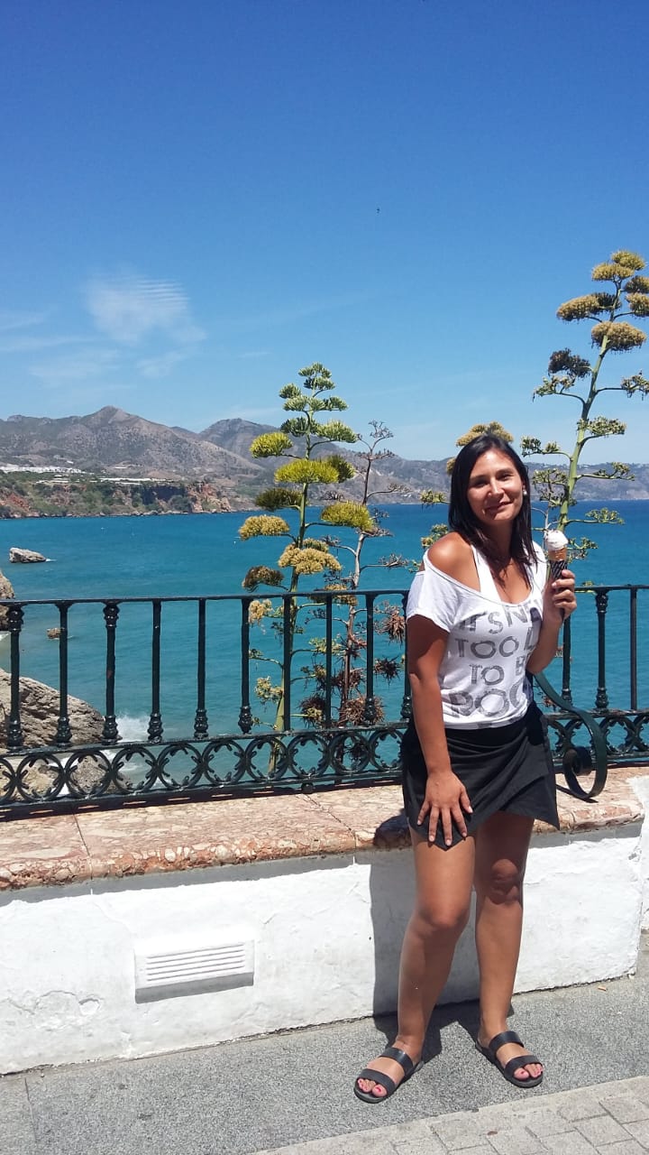 Bruna diante de uma paisagem entre montanhas e mar
